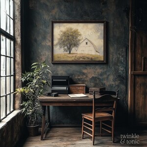 Op de afbeelding: Een rustieke interieursc&egrave;ne met een houten bureau, stoel en een ingelijst kunstwerk met een boom en een schuur. Een potplant staat bij een groot raam. De kamer heeft een donkere, getextureerde muur.