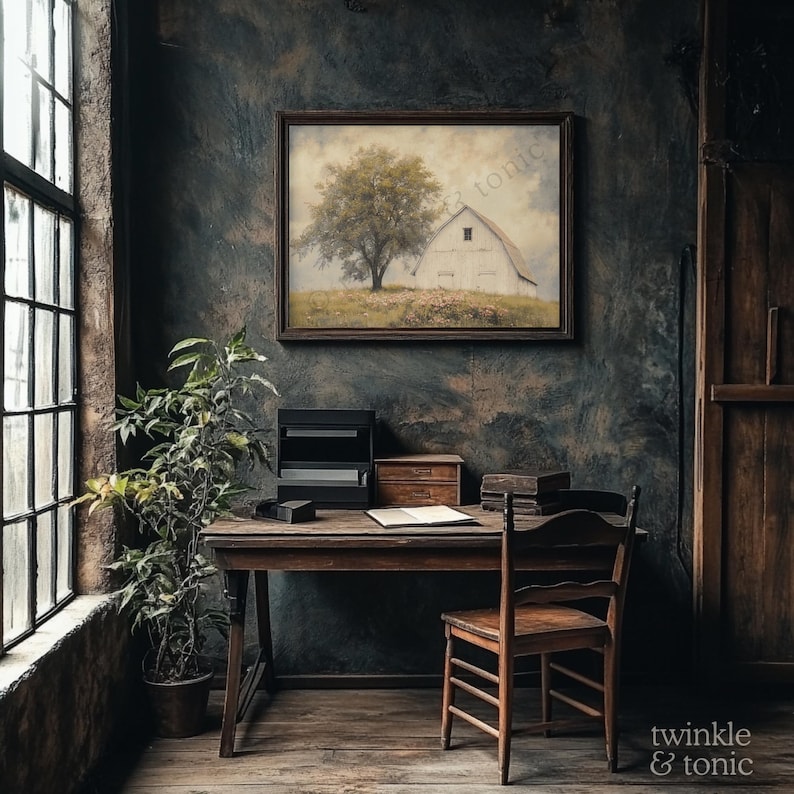 Op de afbeelding: Een rustieke interieursc&egrave;ne met een houten bureau, stoel en een ingelijst kunstwerk met een boom en een schuur. Een potplant staat bij een groot raam. De kamer heeft een donkere, getextureerde muur.