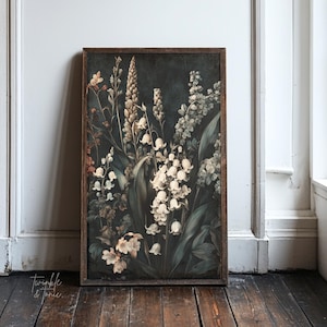 May include: A framed botanical print with a dark backdrop, showcasing white and cream flowers and green leaves. The artwork has a vintage style, with a wooden frame and a distressed appearance. The print is propped against a white wall on a wooden floor.