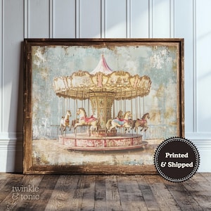 Puede incluir: Impresión enmarcada de un carrusel vintage con caballos. El carrusel tiene un dosel rosa y dorado sobre un fondo azul desgastado. La impresión está en un marco de madera y tiene el texto "twinkle & tonic" en la esquina inferior izquierda.