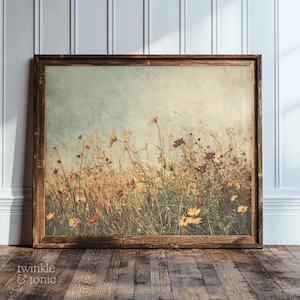 Può includere: Una stampa incorniciata raffigurante un campo di fiori selvatici nei toni del giallo, rosso e marrone. L'opera d'arte ha un'estetica vintage, con uno sfondo di cielo blu tenue. La cornice in legno aggiunge un tocco rustico.