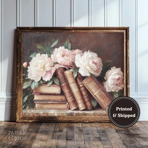 May include: A framed print featuring a still life of books and flowers. The artwork showcases a bouquet of pink and white peonies atop a stack of vintage books. The frame is a warm brown color, and the overall aesthetic is classic and elegant.