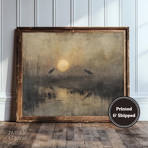 May include: A framed art print depicting a tranquil scene with two herons set against a sunset. The artwork has a vintage style, with a warm colour palette of browns and yellows. The print is in a wooden frame and includes the text "twinkle & tonic".