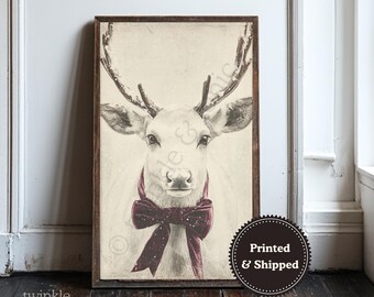 Puede incluir: Una impresión enmarcada de un ciervo blanco con grandes astas y una pajarita burdeos. La obra de arte tiene una estética vintage, con un fondo suave y neutro y un marco marrón oscuro. La impresión está etiquetada como "Printed & Shipped".