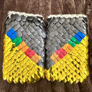 May include: A pair of black and gold fingerless gloves with a rainbow pattern. The gloves are made of small, overlapping scales.