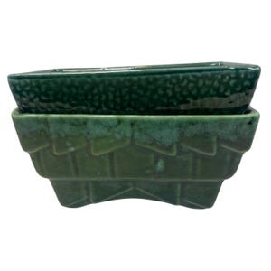 May include: Two green ceramic planters. The top planter is a darker shade of green with a textured surface. The bottom planter is a lighter shade of green with a textured, geometric design. Both planters are rectangular.
