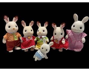 May include: A group of six toy rabbit figures. The rabbits have white fur with brown-tipped ears and are dressed in various outfits. The outfits include a red polka-dot dress, a yellow and green dress, and a plaid shirt with brown trousers.