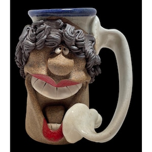 May include: A white ceramic mug with a black handle and the text "But First, Coffee" in a black, bold font. The mug is on a white surface.