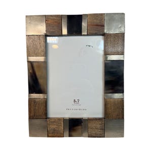 May include: Rectangular photo frame with a mixed material design. The frame features a combination of wood, metal, and dark horn-like accents. The frame is labeled "5x7" and "Pottery Barn".