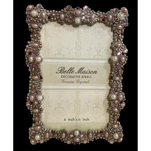 May include: Ornate silver-toned picture frame embellished with faux pearls and pink and red crystals. The frame has the text "Belle Maison Decorative Jewels Genuine Crystals" and is sized at 4 inches x 6 inches.
