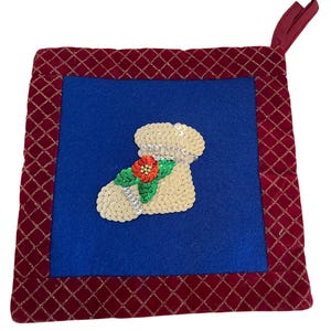 May include: Square Christmas stocking decoration with a blue center and a red, diamond-patterned border. The stocking is embellished with sequins and a red and green floral design. A red loop is attached for hanging.
