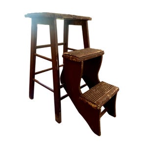 May include: A dark brown wooden step stool featuring a tall back section with four legs and a lower front section with two steps. The wood shows visible signs of wear and paint chipping throughout the entire structure of the stool.