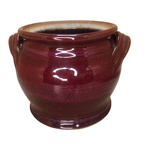 May include: A deep red ceramic pot with two handles. The pot has a glossy finish and a rounded shape.