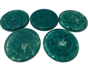 May include: Five teal-colored, round coasters with a speckled pattern. The coasters have a glossy finish and a slightly irregular shape. The teal color is a deep, rich hue, and the speckled pattern adds visual interest.