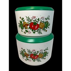 May include: Two white, round kitchen storage bowls with green lids. Each bowl is decorated with a repeating pattern of red tomatoes, green peppers, brown mushrooms, and yellow onions. The bowls are stacked on top of each other.