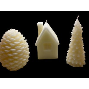 May include: Three ivory-colored candles in the shapes of a pine cone, a house, and a Christmas tree. The candles are unscented and have a smooth, waxy texture. The background is solid black.