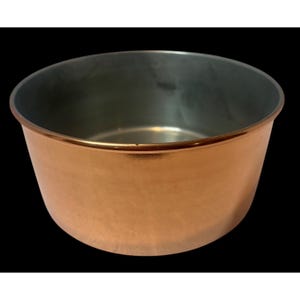 May include: A round, open-top bowl featuring a polished copper-colored exterior finish and a smooth, metallic silver-toned interior surface. The vessel has a simple, wide-rimmed design with a consistent, uniform shape and a reflective metallic texture.