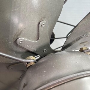 May include: Close-up of a vintage gray electric fan. The fan blades and housing are a muted gray color. The metal frame has the text "PAT.1967257" stamped on it. The fan blades are protected by a wire cage.