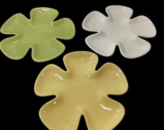 May include: Three flower-shaped ceramic dishes in shades of green, white, and yellow. The dishes have a glossy finish and are arranged against a black background. These decorative dishes are ideal for serving snacks or as decorative accents.