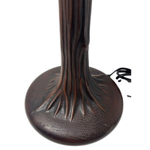 May include: A dark brown lamp base featuring a textured, sculpted design that mimics the appearance of a tree trunk with visible roots spreading across a circular base. A black electrical cord extends from the side of the lamp base.