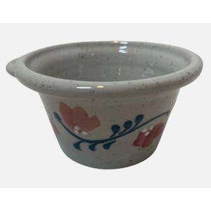 May include: A speckled, light gray ceramic bowl with a wide rim and a small handle. The bowl is decorated with pink floral designs and blue vine-like accents. The bowl is likely used for serving or display.