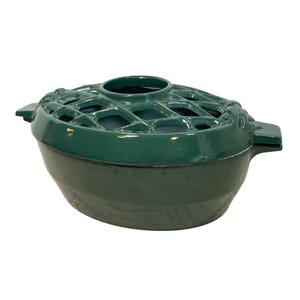 May include: A dark green, oval-shaped cast iron flower frog with a lattice top and two side handles. The flower frog is designed to hold floral arrangements and has a glossy finish.