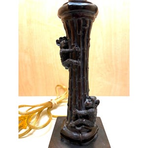 May include: A dark brown lamp base with a bamboo-style column, featuring two detailed monkey figurines climbing the column. The lamp has a square base and a decorative top, with a gold-colored electrical cord.