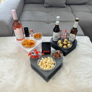 Könnte beinhalten: Herzförmige Serviertabletts mit Snacks und Getränken, darunter eine Flasche Roséwein, Limonade und Bier. Die Tabletts enthalten Chips, Erdnüsse, Popcorn und Pralinen. Ein Smartphone zeigt das Netflix-Logo.