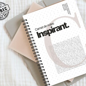 Peut inclure: Un carnet de notes à spirales blanc avec le mot "Inspirant" en gras sur la couverture. Le carnet a un accent rose clair et un tampon "FAIT AU QUÉBEC". Le carnet est posé sur une surface grise.