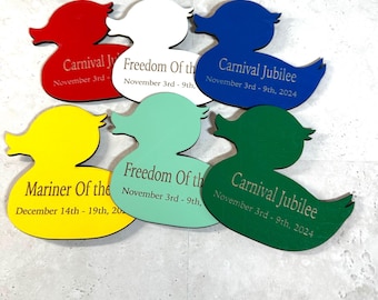 May include: A collection of six duck-shaped wooden cutouts in various colors: red, white, blue, yellow, mint green, and green. Each duck features engraved text with event names and dates. The ducks are arranged on a light gray surface.