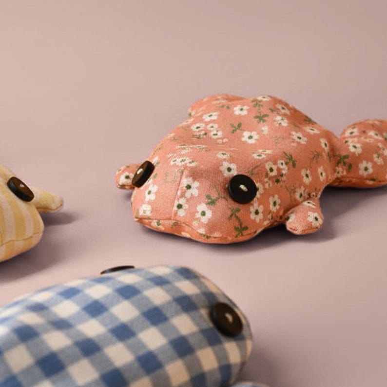 May include: Three handmade fabric fish toys. One is peach-colored with a white floral pattern, another is yellow with vertical stripes, and the third is blue and white checkered. Each has large black button eyes.