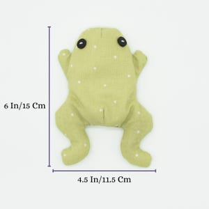 May include: A handmade green frog plush toy with white polka dots. The frog has black button eyes and outstretched limbs. It measures 6 inches (15 cm) in length and 4.5 inches (11.5 cm) wide.