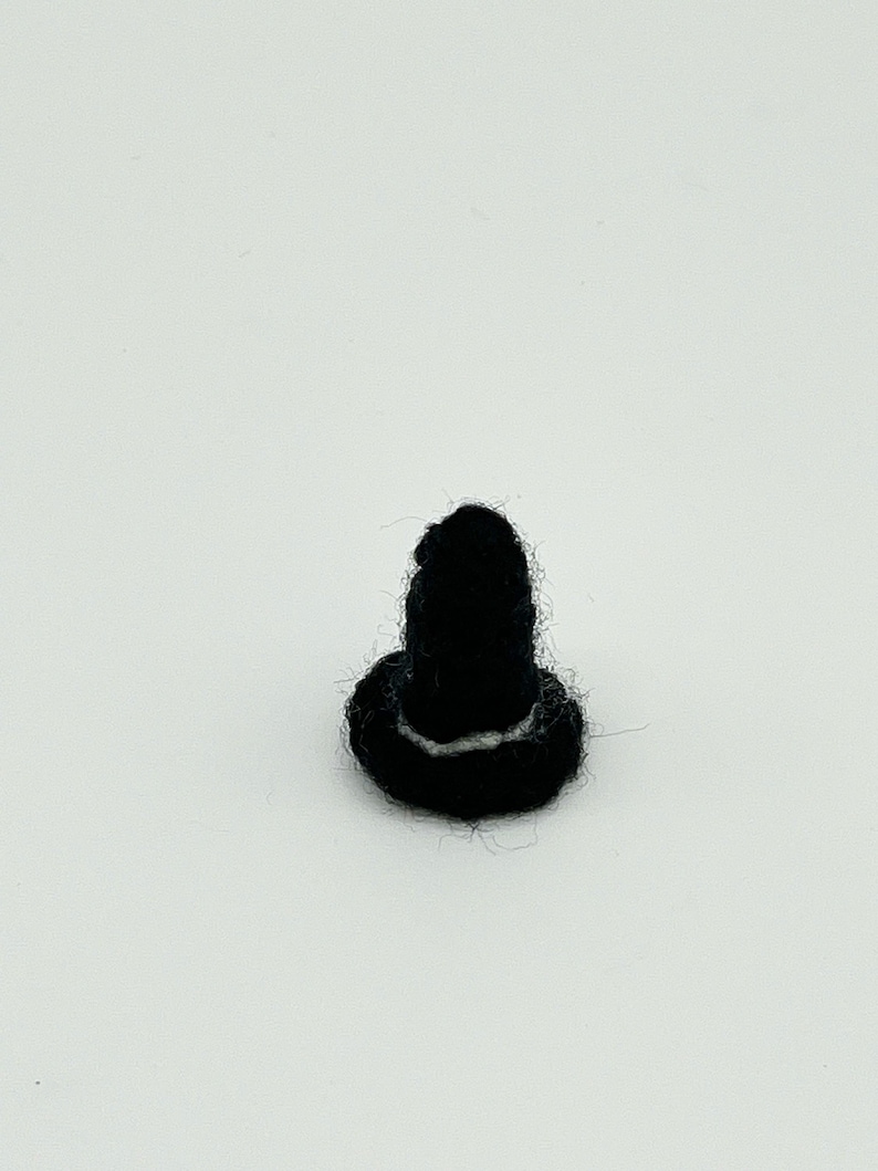 Op de afbeelding: Een zwarte knoop van vilt met een witte ring rond de bovenkant.