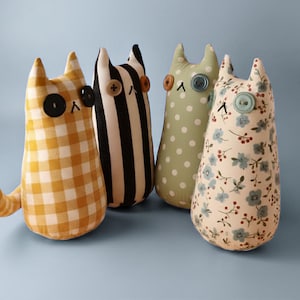 May include: Four stuffed cat dolls with button eyes and stitched features. The cats have different patterned fabrics: yellow gingham, black and white stripes, green polka dots, and floral print. Each cat has a button for a nose.