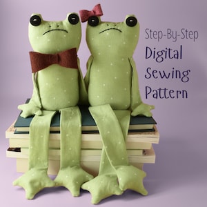 Puede incluir: Dos ranas de tela verde claro con lunares blancos, ojos de botón negros y patas largas. Una rana lleva una pajarita de fieltro marrón, la otra un pequeño lazo de fieltro rosa. Texto: Step-By-Step Digital Sewing Pattern. Sentadas sobre libros.