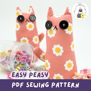 May include: Two handmade pink cat-shaped plush toys with daisy patterns and black button eyes. The image also shows a clear container with colorful sewing clips and the text "EASY PEASY PDF SEWING PATTERN".