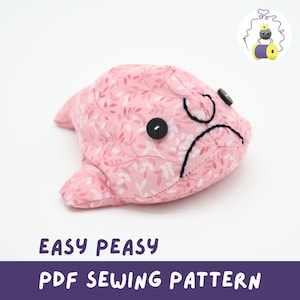 Könnte beinhalten: Ein rosa Stoff-Fisch-Plüschtier mit floralem Muster, schwarzen Knopfaugen und einem aufgestickten Stirnrunzeln. Der Text "EASY PEASY PDF SEWING PATTERN" wird darunter angezeigt. Ein kleines Logo mit Krone und Nähfaden befindet sich oben rechts.