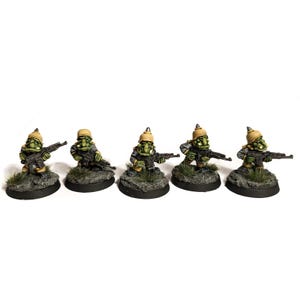 Könnte beinhalten: Fünf Miniaturfiguren von goblinartigen Kreaturen in Militäruniform. Jede Figur ist grün mit einem beigefarbenen Helm und hält ein Gewehr. Sie stehen auf kleinen, runden, grauen Sockeln mit grünen Pflanzenbüscheln.