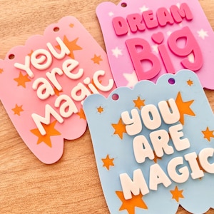 May include: Three colorful banner-shaped decorations with inspirational messages. One pink banner reads "You are Magic" with orange star accents. Another pink banner says "Dream Big." A blue banner also reads "You are Magic."