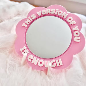 Może przedstawiać: Biały ceramiczny kubek z czarnym uchwytem i napisem "But First, Coffee" czarną, odręczną czcionką. Kubek stoi na białej powierzchni.