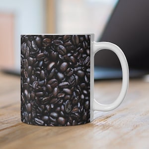 Puede incluir: Taza de café de cerámica blanca con una imagen de primer plano de granos de café marrones oscuros.