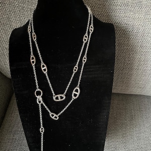 Puede incluir: Collar plateado con diseño en capas. El collar presenta una serie de eslabones ovalados conectados por delicadas cadenas. Una cadena más larga con cierre en T cuelga hacia abajo, creando una forma de Y.