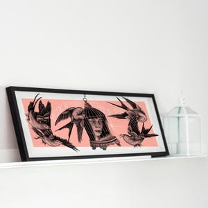 May include: Framed art print featuring a woman's face inside a birdcage, surrounded by flying birds. The artwork has a black and white illustration style with a pink background. The frame is black and the print is displayed on a white shelf.