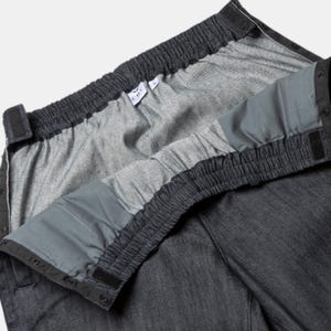 K&ouml;nnte beinhalten: Eine dunkelblaue Jeanshose mit elastischem Bund und verstellbaren Tr&auml;gern. Der Bund ist umgedreht, um den Gummizug und die Tr&auml;ger zu zeigen.