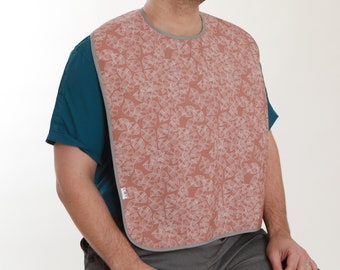 Pode incluir: Um babador rosa com um padrão geométrico branco. O babador tem uma borda cinza ao redor das bordas.