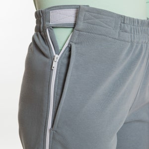 May include: Gray sweatpants with a white zipper detail running down the side seam. The waistband has a white elastic band and a white adjustable strap.