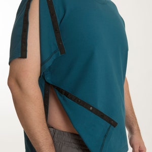 Pode incluir: Uma t-shirt de manga curta em verde azulado com detalhes de fita preta vertical com botões de pressão ao longo do ombro e da costura lateral. A peça tem gola redonda e um design aberto na lateral e na manga.