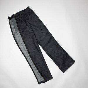 K&ouml;nnte beinhalten: Eine dunkelblaue Jeanshose mit einem einzigartigen Design, das eine Rei&szlig;verschluss&ouml;ffnung an der Seitennaht aufweist. Die Hose hat einen Knopfverschluss und eine lockere Passform.
