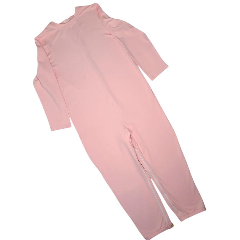 Pode incluir: Um macac&atilde;o de manga comprida em rosa claro, com decote redondo e pernas compridas. A pe&ccedil;a &eacute; feita de um tecido liso e uniforme, incluindo um fecho de correr vertical que se estende do centro do peito at&eacute; &agrave; zona da entreperna.