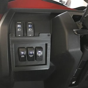 May include: Black panel with three rocker switches labeled "ROCK LIGHTS", "INTERIOR LIGHT", and "BED LIGHTS". Above are two sets of switches labeled "OUTER" and "INNER". The panel is mounted on a vehicle dashboard.
